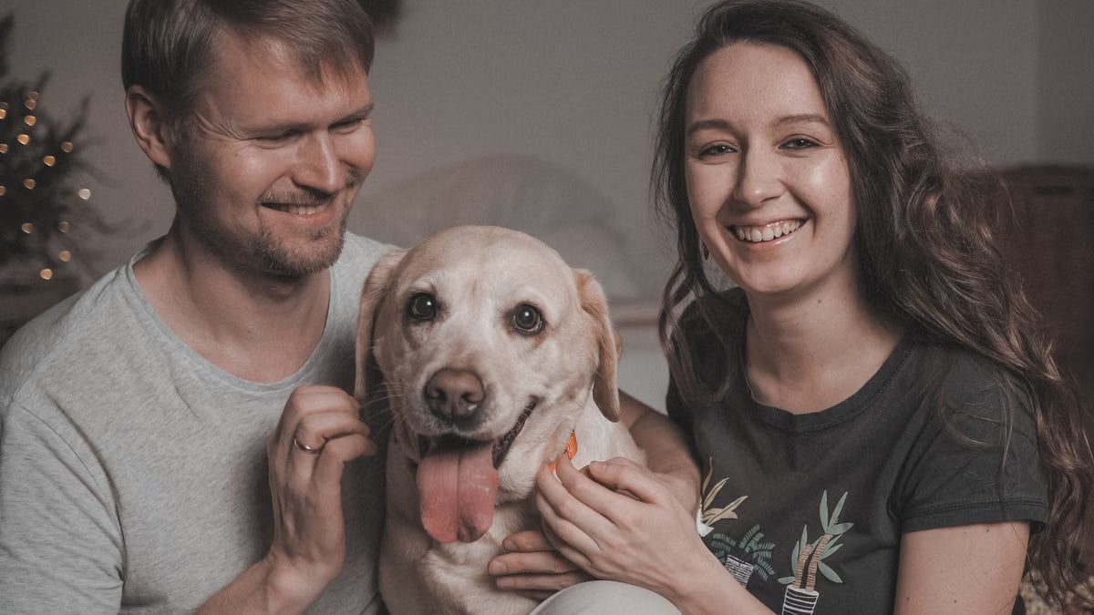 Happy couple playing with their Labrador dog at home, showcasing love and companionship.